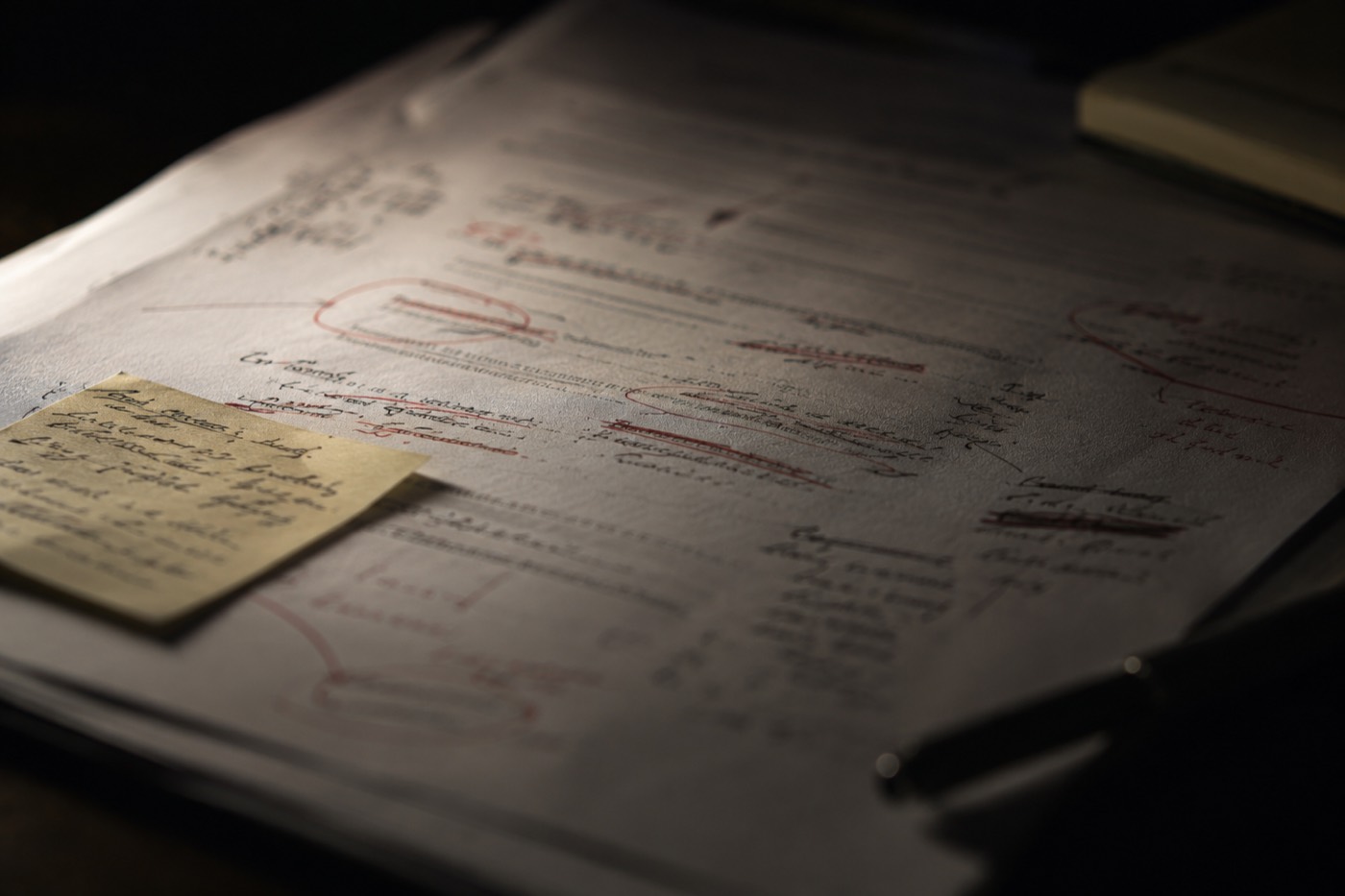 A printed deal document marked up by hand in red pen, a yellow sticky note attached β the reconciliation work that consumes a management team's judgment.