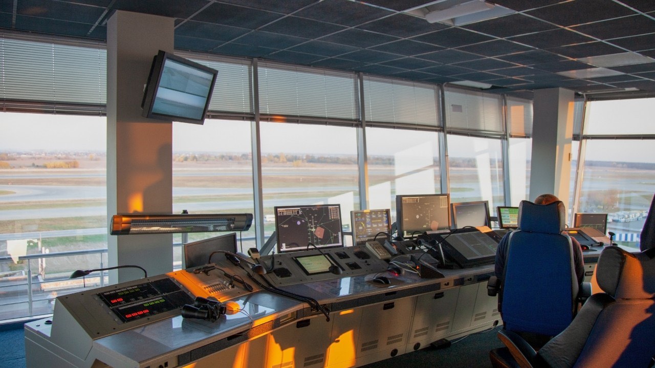An air-traffic control tower cab overlooking a runway, ringed with monitors and consoles — a high-reliability coordination environment.